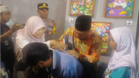 Bupati Jombang, Warsubi membubuhkan tanda tangan pada secarik kertas sebagai apresiasi terhadap permintaan siswi SDN II Kepanjen, peserta pameran lukis Membentang Ijo-Abang #10 di GOR Jombang, Rabu malam, 30 Juli 2025. Foto: kredonews.com/priyo suwarno