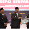 Bupati Jombang Warsubi, didampingi wakil Salmanudin Yazid menyerahkan tanda penghargaan kepada Kurnia Putri Utomo, dari Dinas Kominfo Jombang, sebagai ASN berprestasi di lingkungan pemkab Jombang, Minggu 17 Agustus 2025. Foto: Diskominfo Jombang