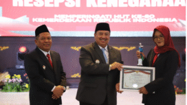 Bupati Jombang Warsubi, didampingi wakil Salmanudin Yazid menyerahkan tanda penghargaan kepada Kurnia Putri Utomo, dari Dinas Kominfo Jombang, sebagai ASN berprestasi di lingkungan pemkab Jombang, Minggu 17 Agustus 2025. Foto: Diskominfo Jombang